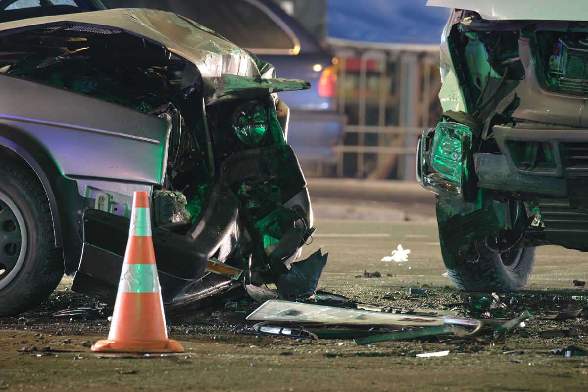 Damaged in heavy car accident vehicles after collision on city street crash site at night. Road safety and insurance concept.