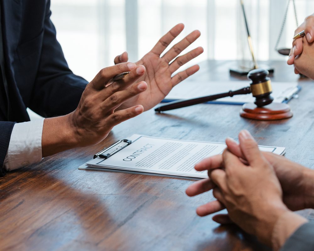 Lawyer explaining contract terms to client using persuasive hand gestures, with contract, gavel and scale on wooden table